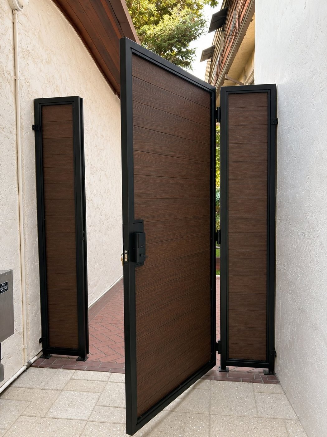 Three-panel composite steel gate open from exterior, matte black welded frame between stucco walls with keypad smart lock - ProHands